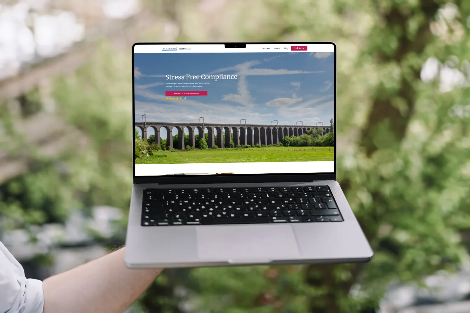 In a garden, a person holds up a laptop with a website displayed.